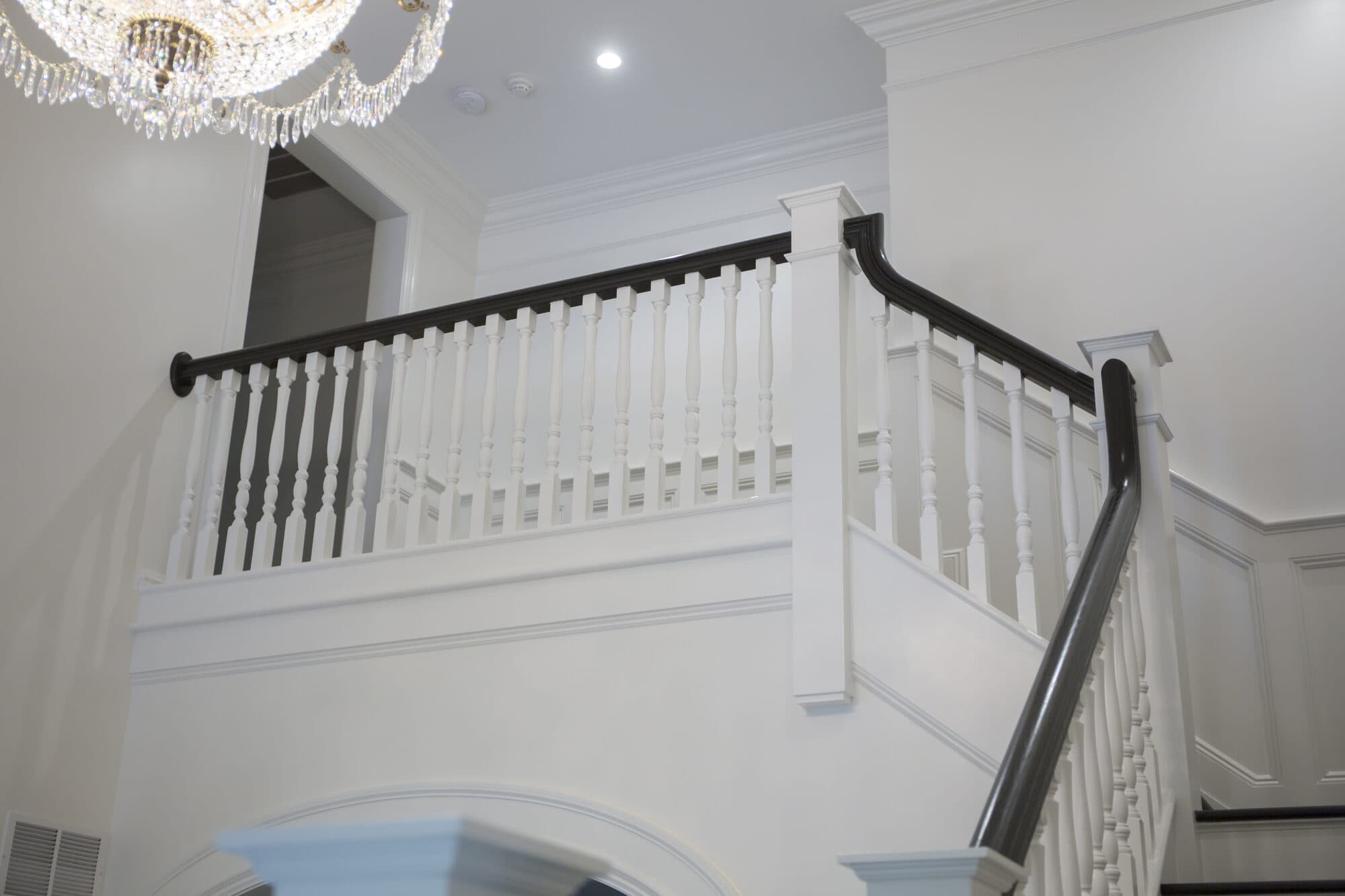 Second-floor balcony rail in white turned balusters and a dark handrail beneath a crystal chandelier
