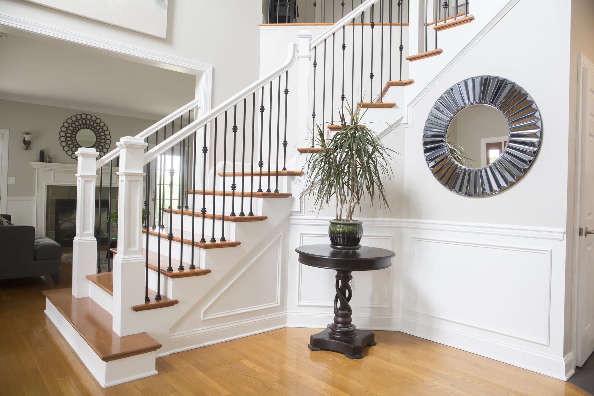 Two-story foyer stair with oak treads, white box newels and black knuckle iron balusters beside a fireplace