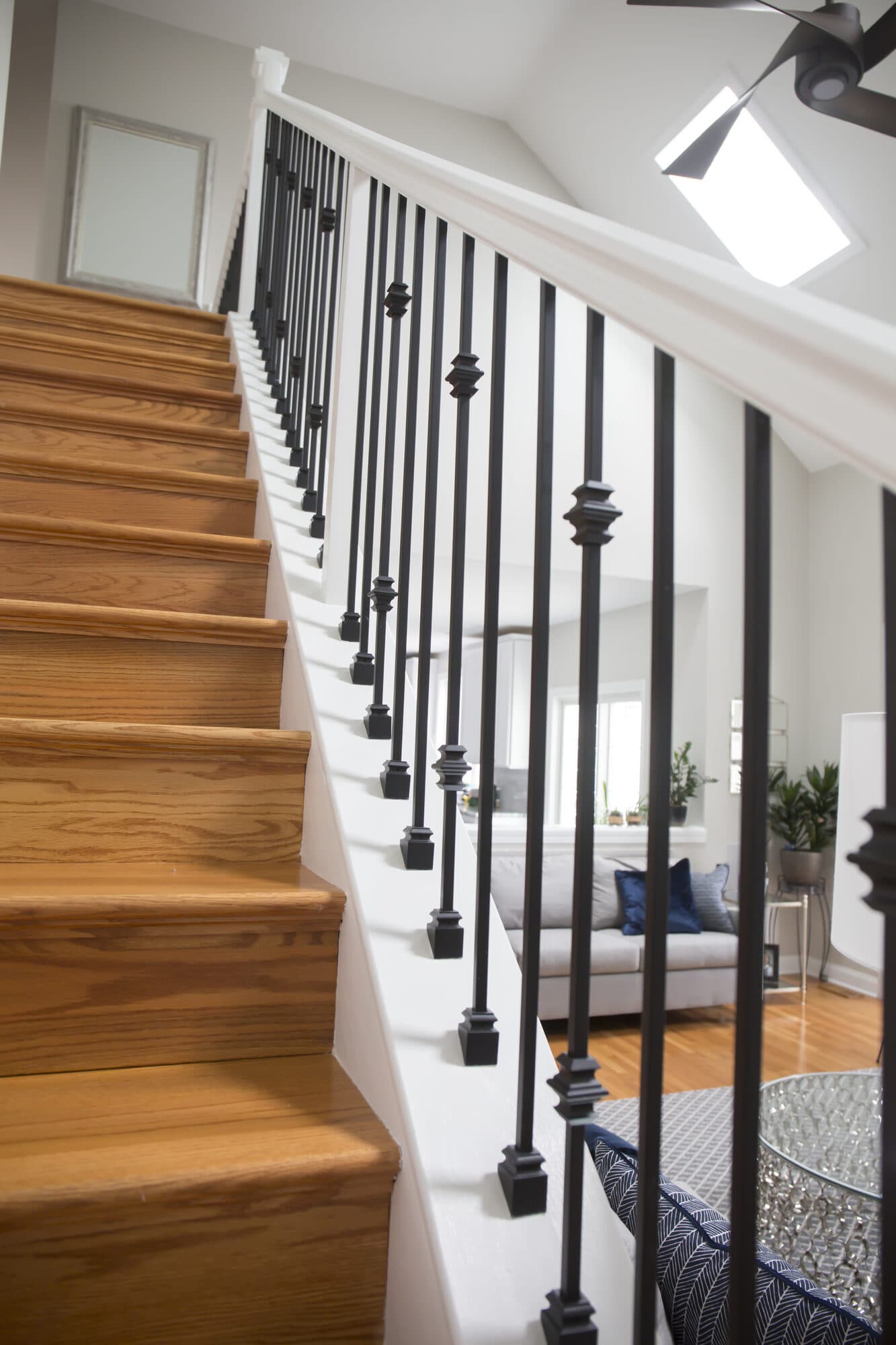 Oak treads with white risers and satin-black knuckle iron balusters climbing toward a vaulted ceiling