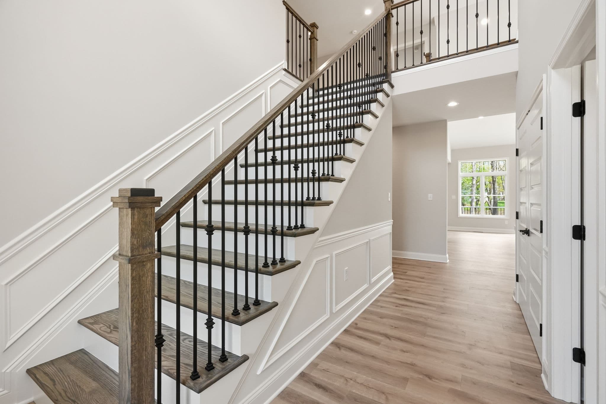 Full custom stair with iron balusters, stained treads, and raised-panel wainscoting — recent Snyder install