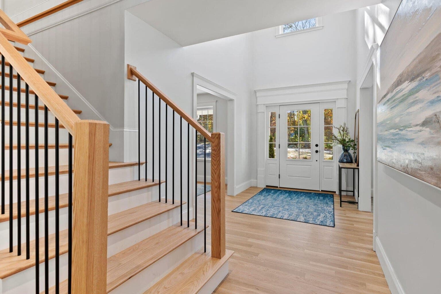 White oak stair and railing with slim black iron balusters in a bright foyer