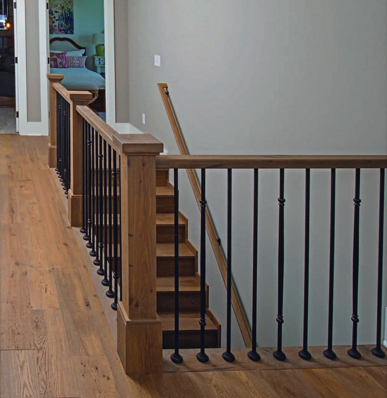 White oak handrail over satin-black iron balusters at a balcony run