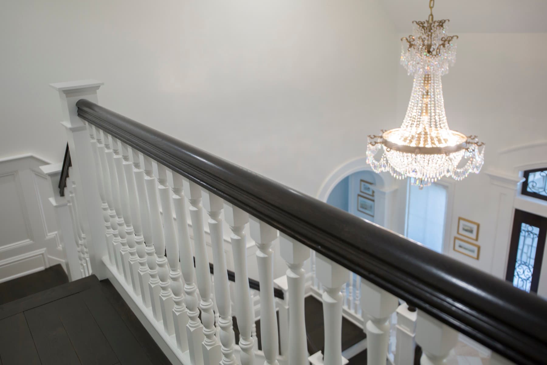 Ebonized handrail over white turned balusters on a balcony with a chandelier above — Caruso residence