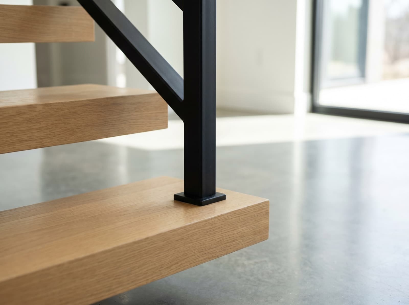 Installed plain square satin-black iron newel on white-oak floating treads in a modern foyer