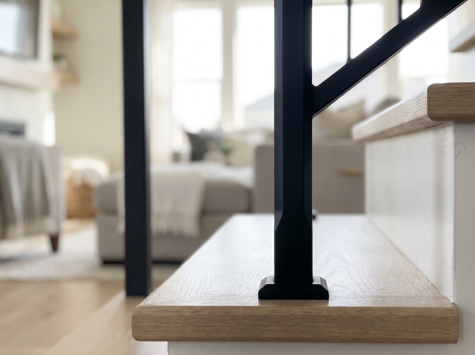 Installed satin-black square iron newel post with chamfered edge on a white-oak tread