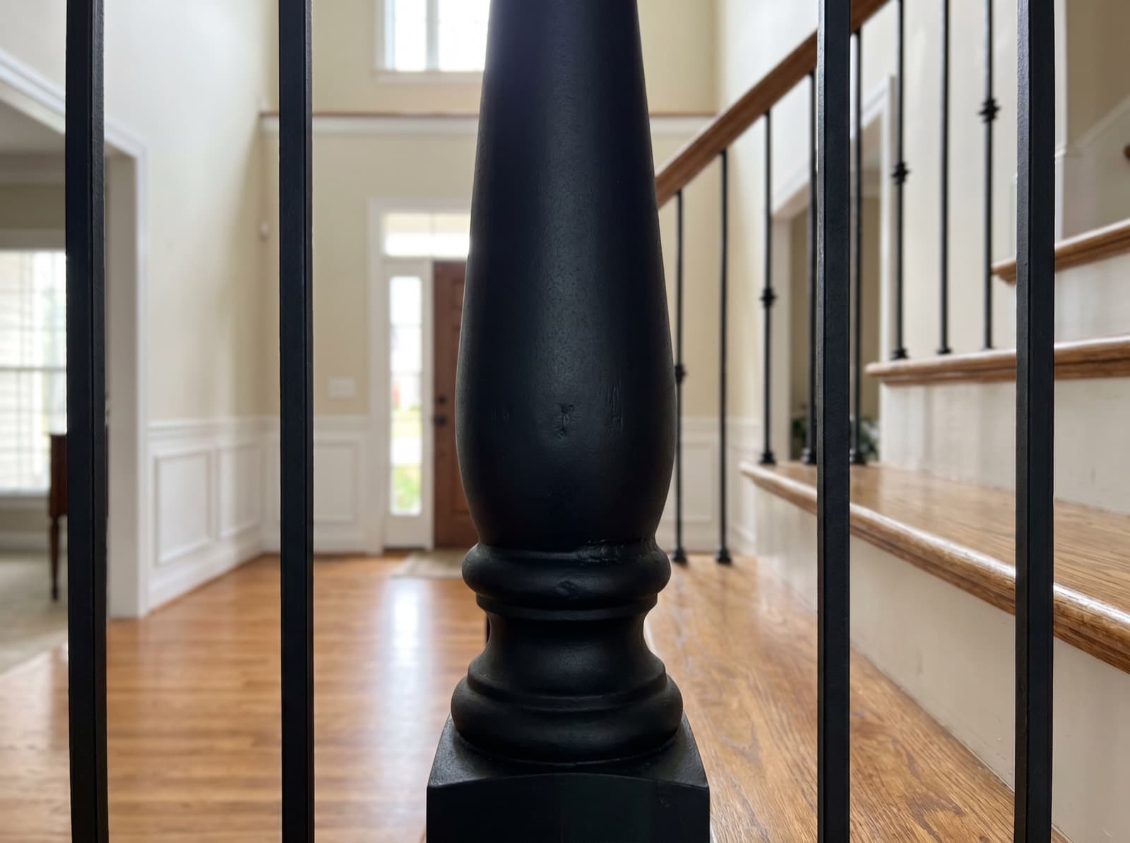 Installed oversized satin-black iron newel accent against standard balusters in a two-story foyer