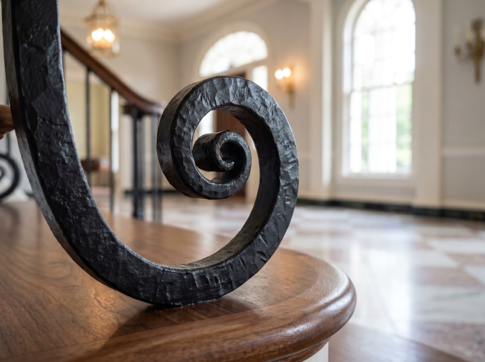 Installed satin-black iron scroll-curl detail on a wood newel cap in a grand foyer