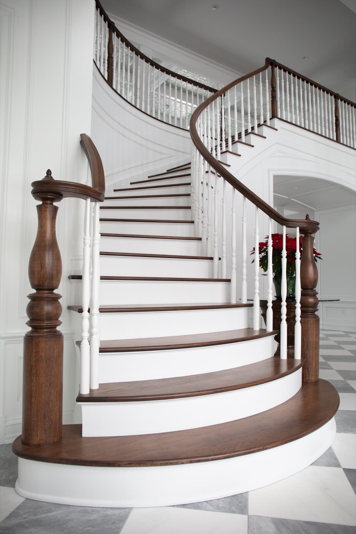 Sweeping curved walnut staircase with white turned balusters and dark newels in a marble foyer — Rambo residence