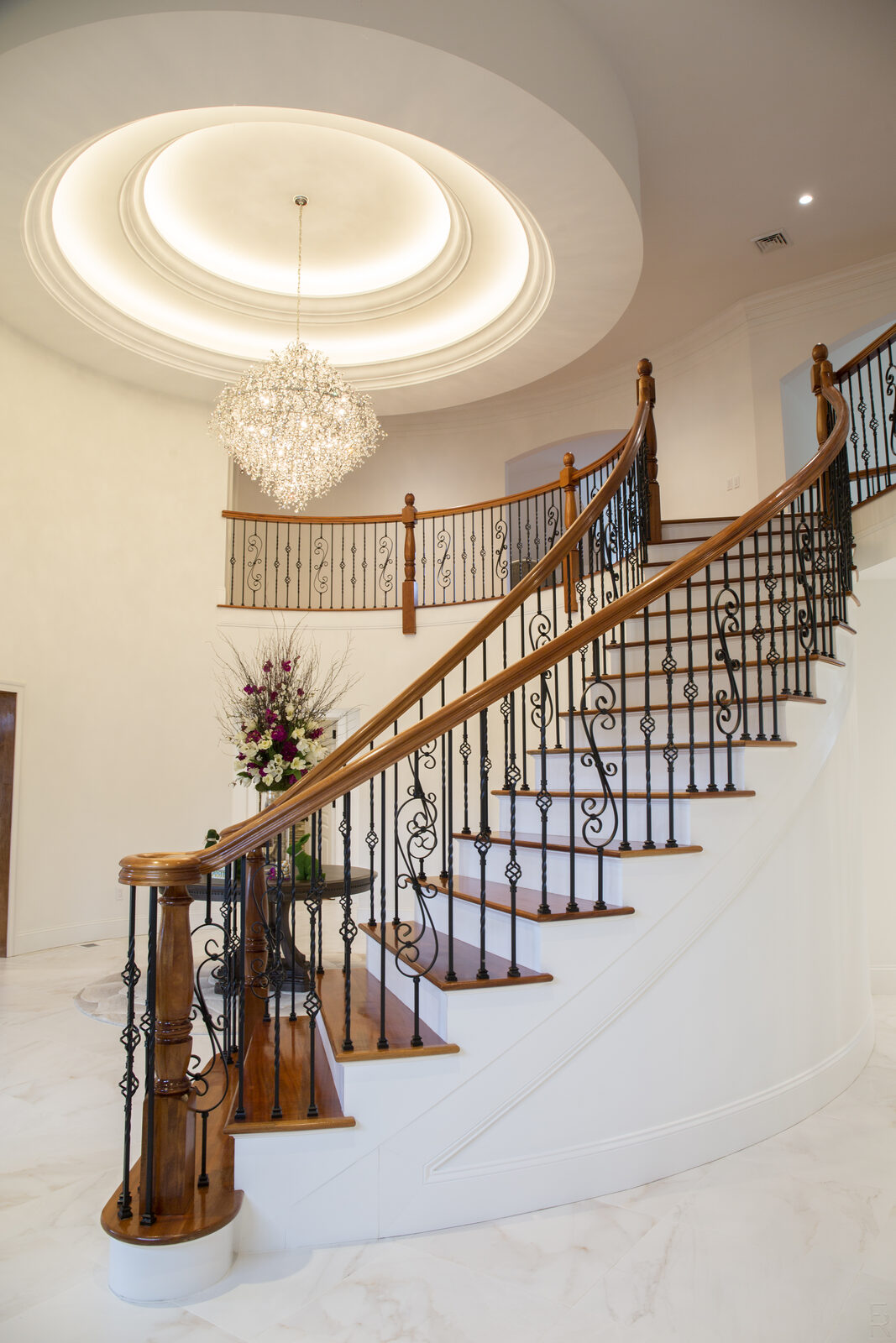 Curved foyer staircase with iron balusters under a chandelier — Snyder Stairs work in the Lehigh Valley.